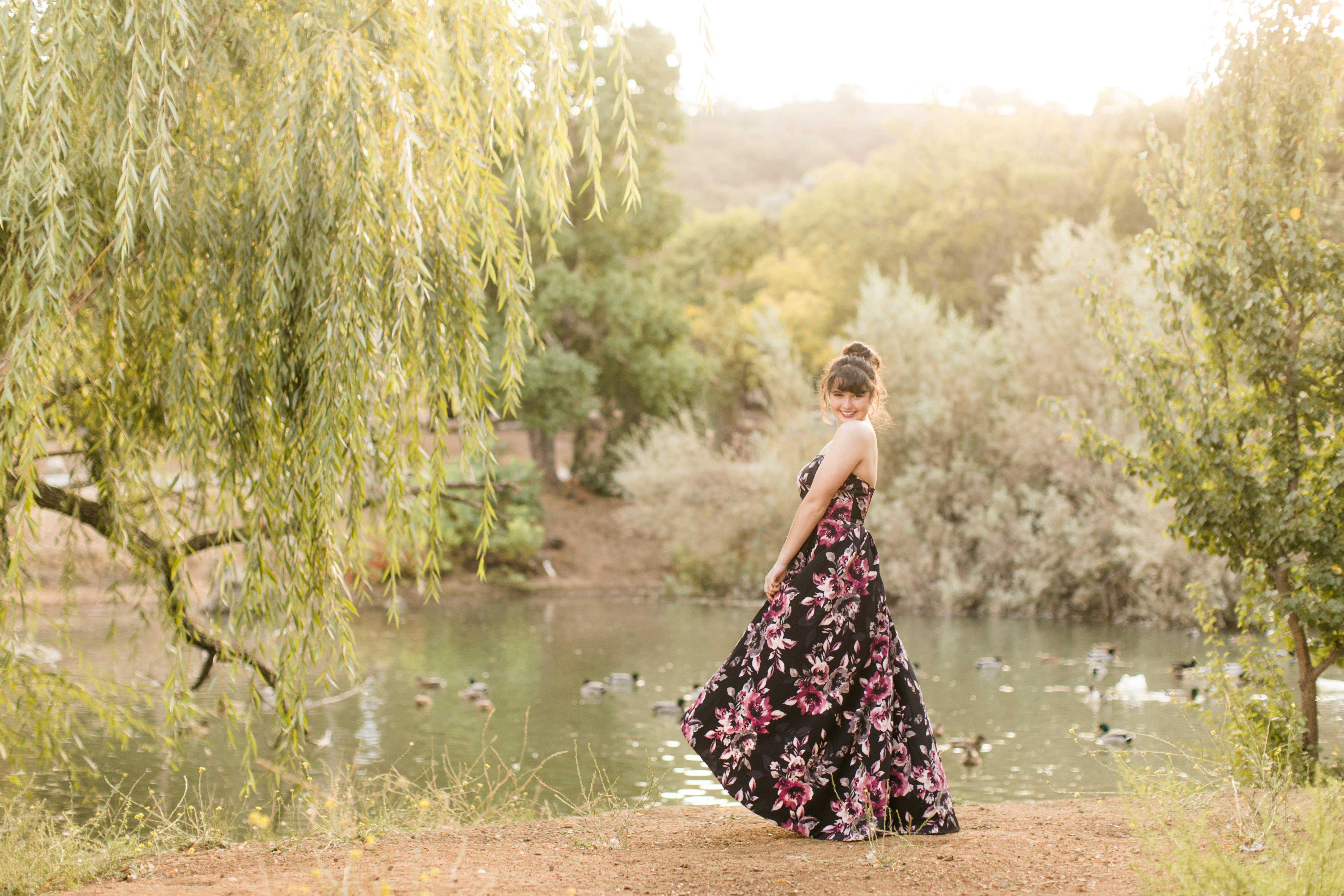 young woman high school senior girl in graduation dress twirling in front of Gavilan College duck pond for senior portraits
