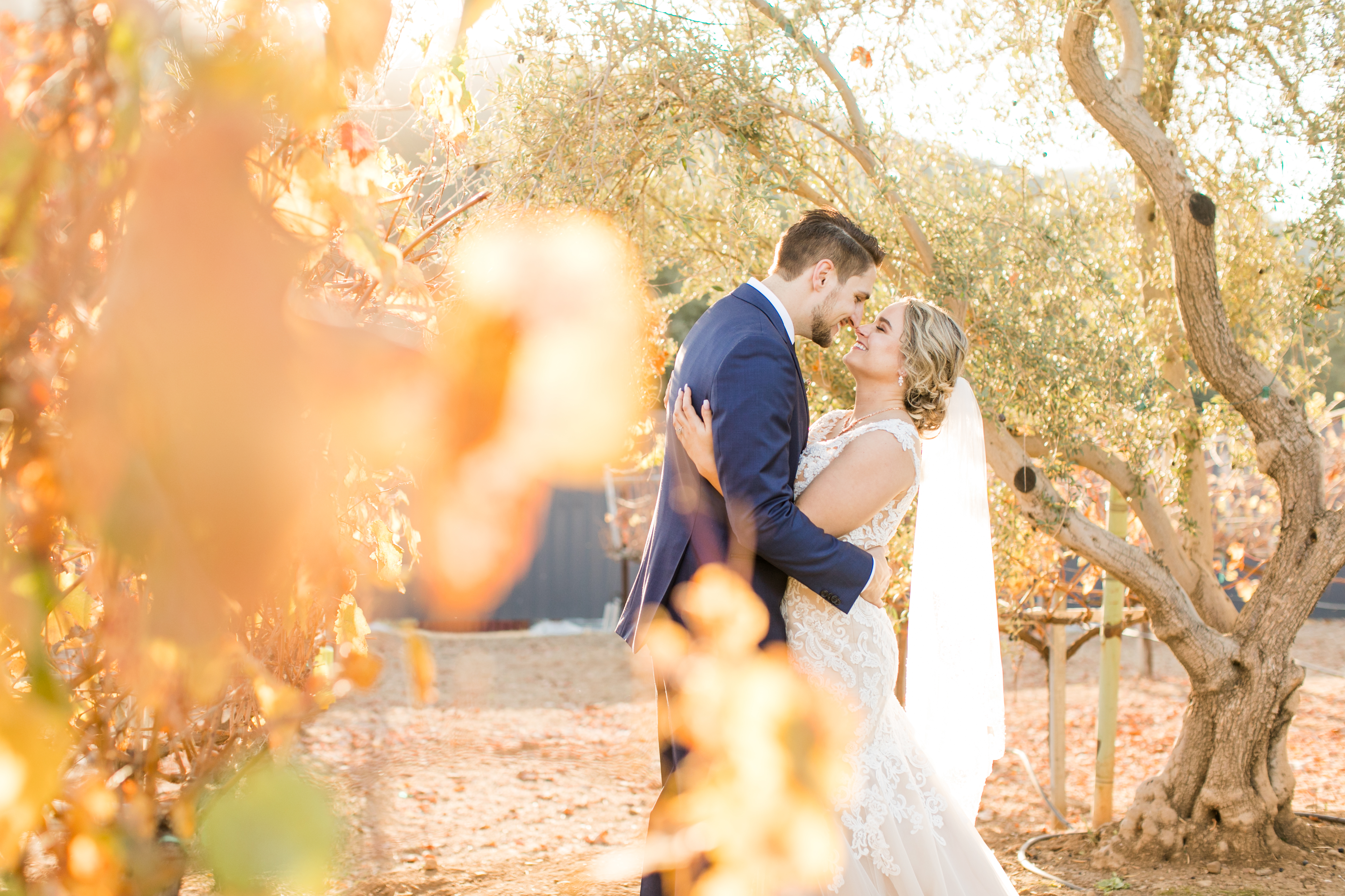 husband and wife in wedding suit and wedding dress during golden hour - couple facing each other in loving embrace with noses touching and smiling at each other