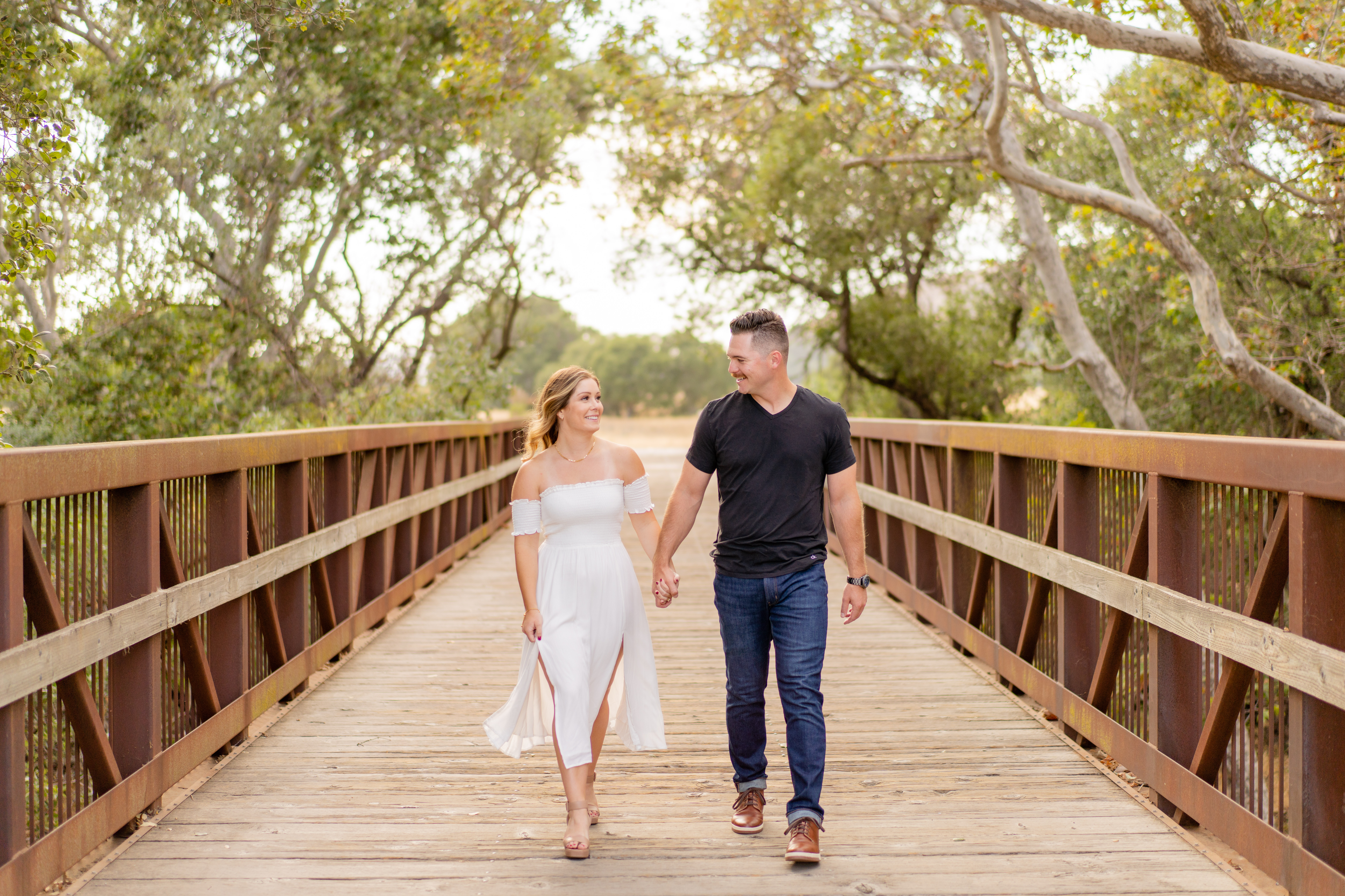 engaged couple walk hand in hand down wooden bridge
