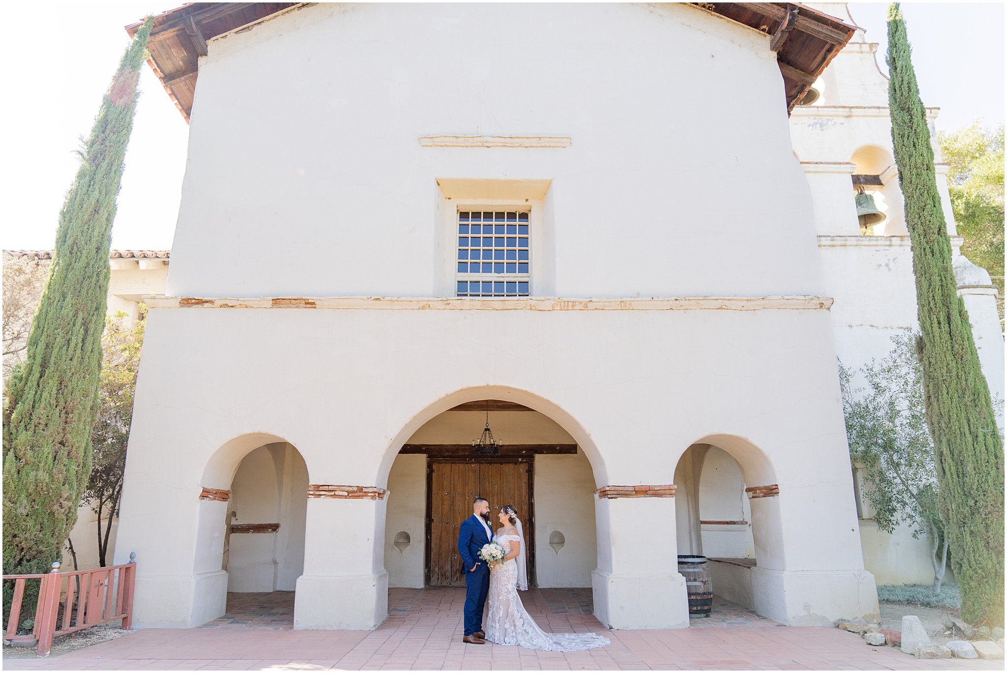 newlyweds stand in an embrace under the arches of an old mission