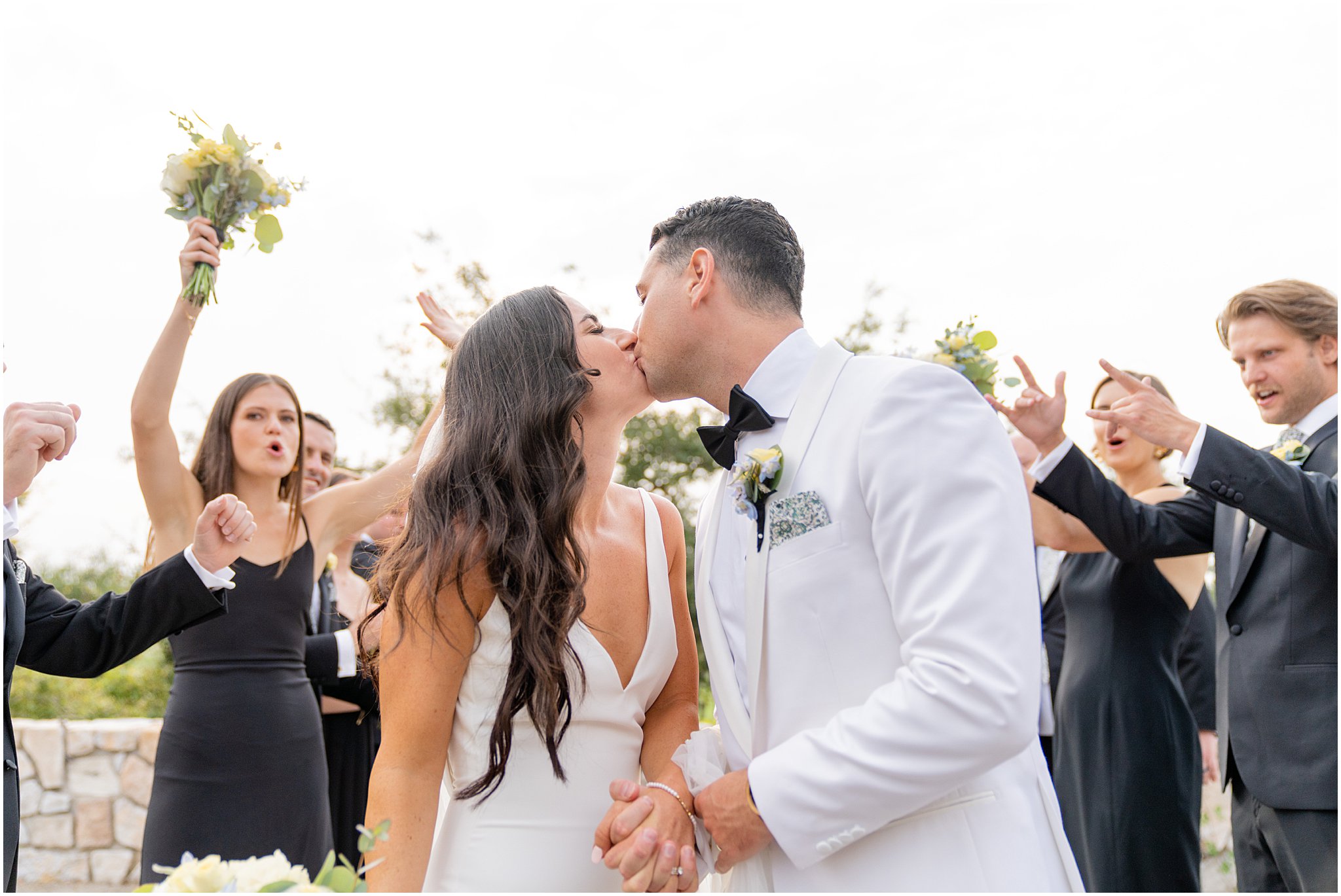 newlyweds kiss with wedding party cheering them on around them