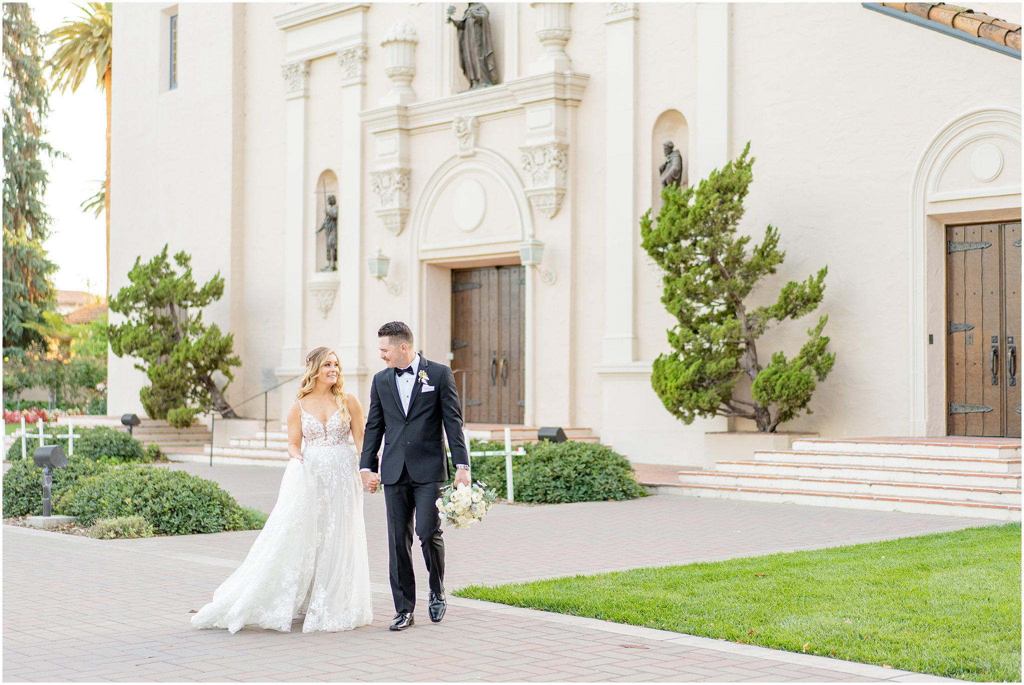 newlyweds walking hand in hand in front of Mission Santa Clara
